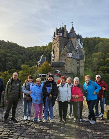 Group of tourists in front of a medieval castle surrounded by forest.