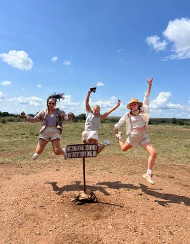 Three people jumping near a sign on a grassy landscape.