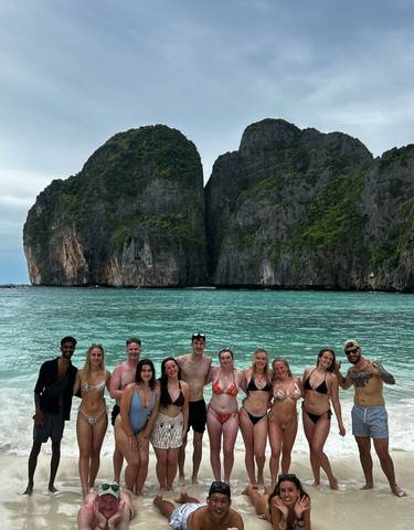 Group of young people standing in the water with large cliffs in the background.