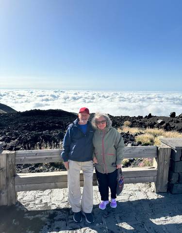 Couple standing on a wooden deck above a sea of clouds.