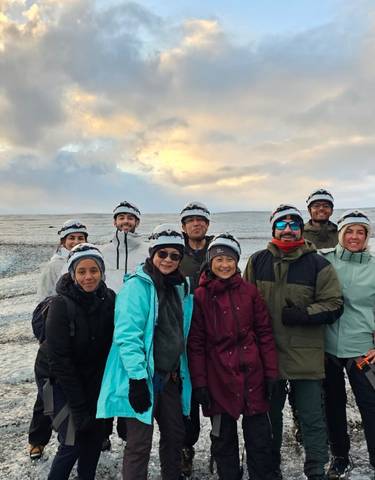 Group of people with helmets standing on a glacier under a cloudy sky.