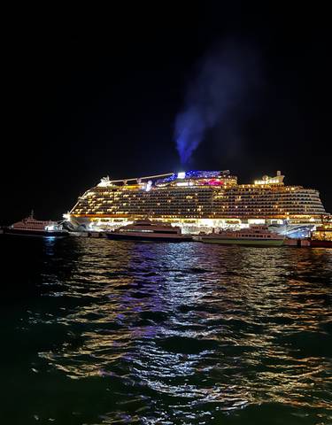 A large lit cruise ship docked at night, reflecting on the water.