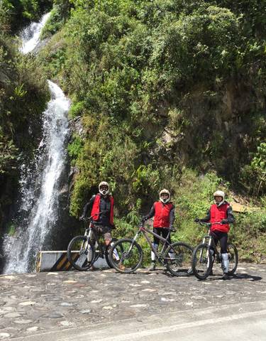 Cyclists wearing helmets posing in front of a waterfall.