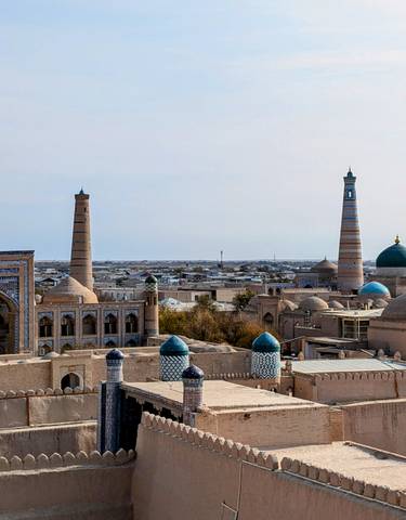 Panoramic view of Khiva with minarets and domed buildings under a clear sky.