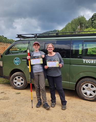 Two people holding certificates in front of a tourist van.