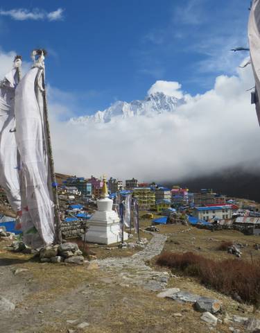 Prayer flags and a mountain village overlooking a snow-capped peak.
