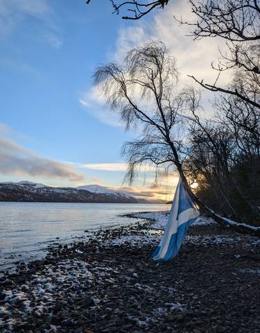 Scottish flag next to a scenic loch with mountains.
