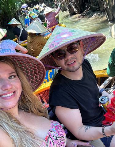 A group of people in a boat with traditional hats rowing through a canal.