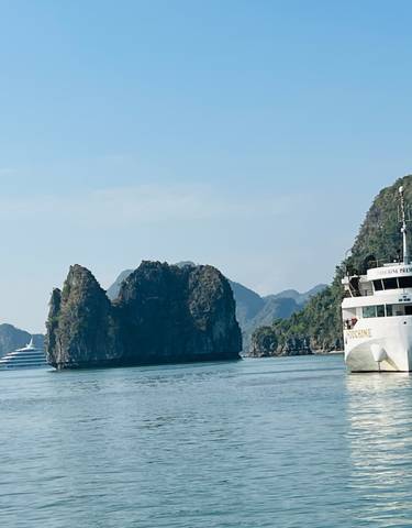 A large ship cruising near limestone formations in a bay.