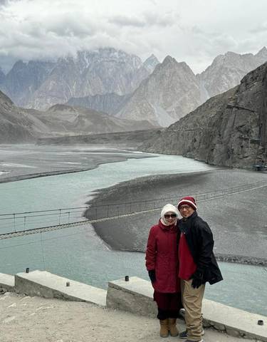 Couple posing in front of a scenic mountain river with a suspension bridge.