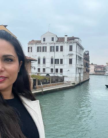 Person posing next to a canal with buildings in the background.