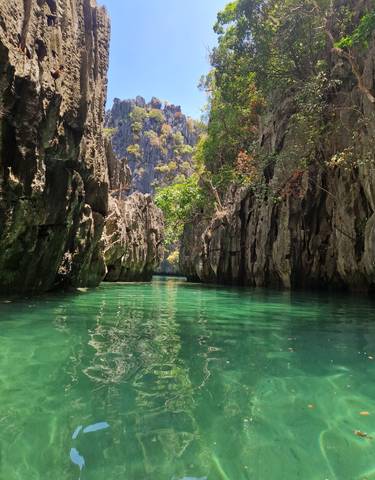 A view of a narrow lagoon flanked by towering rock formations and green foliage.