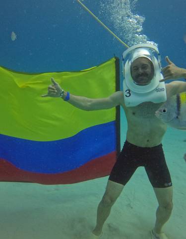 Person underwater with a helmet, a Colombian flag, and fish swimming around.