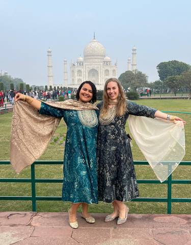 Two women posing in front of the Taj Mahal wearing traditional attire.