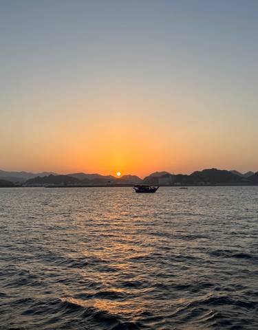 Sunset over a body of water with a boat silhouetted in the foreground.