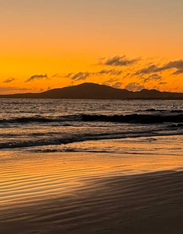Beautiful sunset over a beach with a lighthouse and ocean waves.