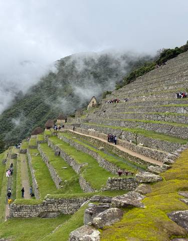 Terraced ruins with people walking on the pathway, surrounded by mist.