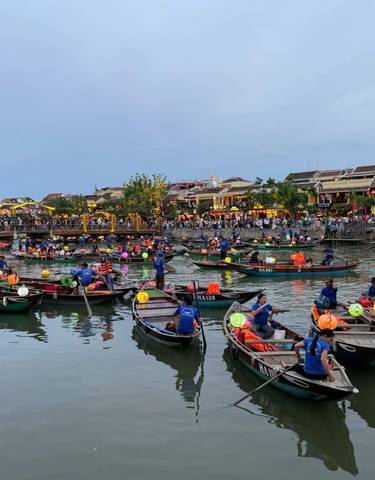 Busy river with boats and people, vibrant town in the background.