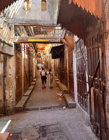 Two people walking through a narrow alleyway in a traditional Moroccan market.