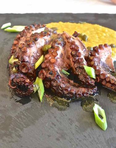 Close-up of a gourmet octopus dish with garnish on a slate platter.