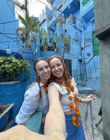 Two people smiling and posing in front of blue-painted buildings.