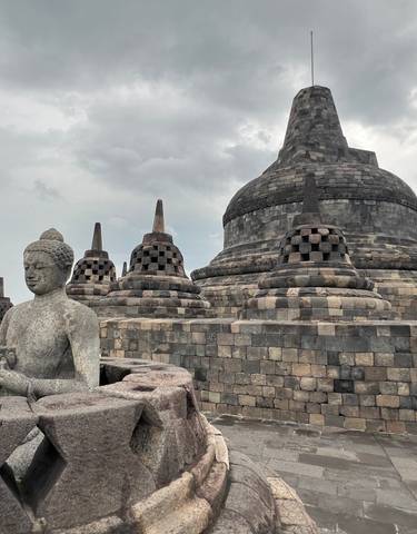 Statues and stupas at Borobudur with a person in traditional attire.