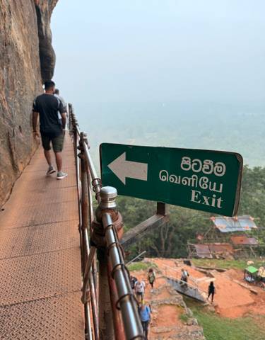 A person walking on a pathway next to a cliff, with an exit sign in multiple languages.