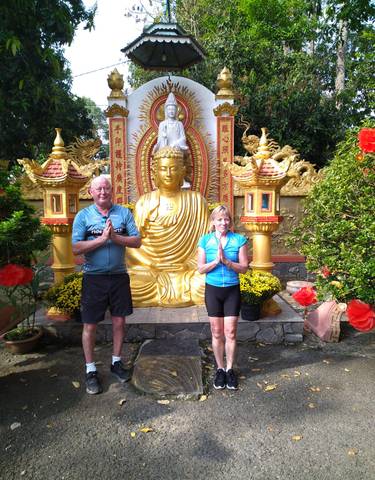 Two people posing in front of a golden Buddha statue.