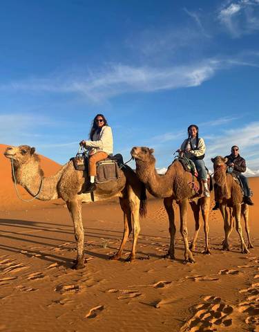 Three people riding camels in a desert setting.