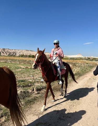 Person riding a horse on a dirt path with rocky hills in the background.