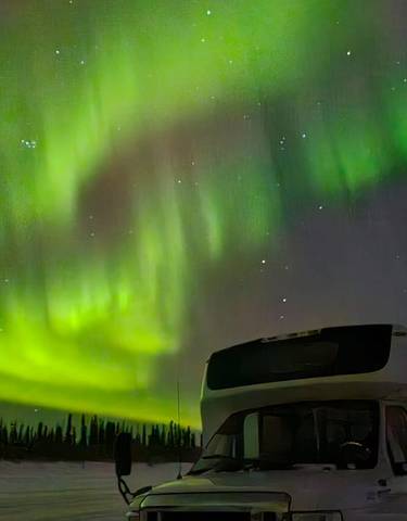 Northern lights over a bus in a snowy landscape at night.