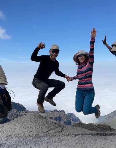 Four people jumping on a mountain with a cloudy sky and distant landscape.