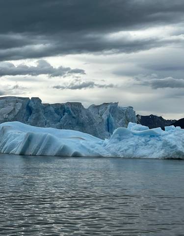 Large iceberg floating in calm waters under a cloudy sky.