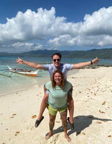 Couple posing on a tropical beach with clear water and traditional boat.