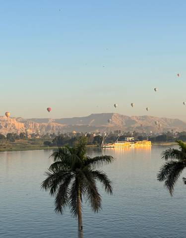 Hot air balloons over a river and mountains at sunrise.