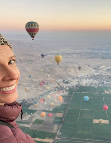A person in a hot air balloon over a landscape with other balloons.
