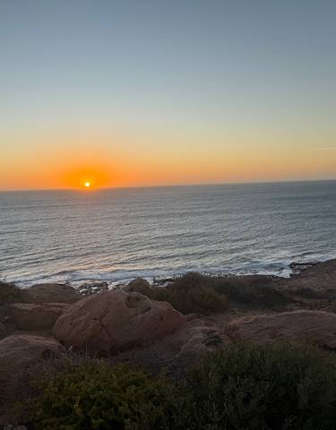 Sunset over the ocean with a rocky coastline.
