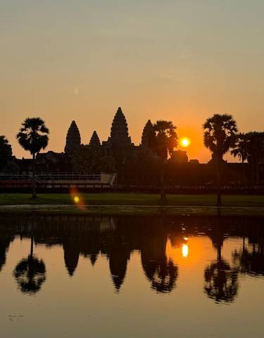 Silhouetted Angkor Wat temple complex with sunset in the background.