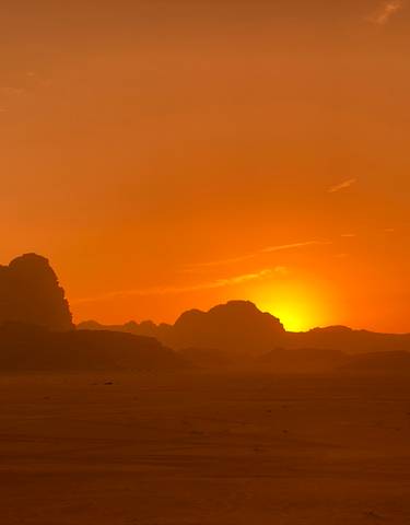 Sunset over desert landscape with silhouetted rocks.
