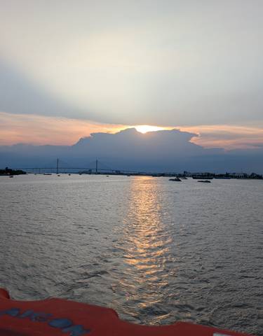 Sunset over a river with boats and a bridge in the distance.