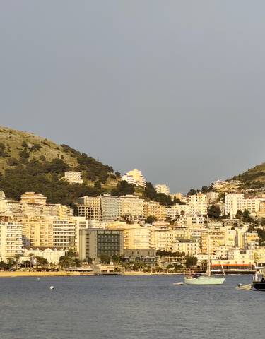 Coastal cityscape with boats and buildings against a mountainous backdrop.