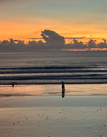 A scenic beach sunset with people walking on the shore.