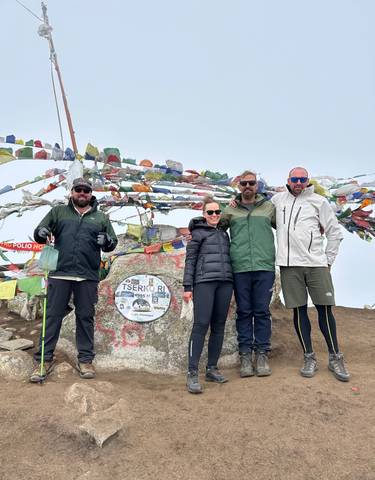 Hikers posing with prayer flags on a mountain summit.