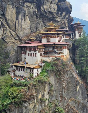 Monastery perched on a cliff surrounded by lush greenery.