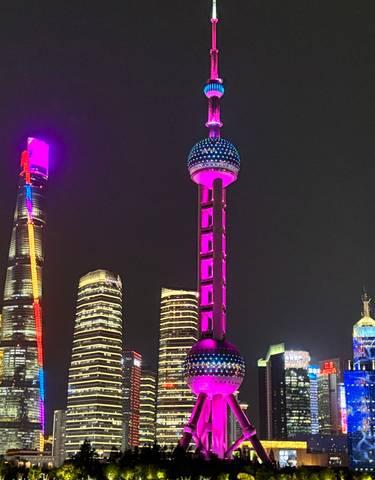 Night cityscape showing colorful illuminated skyscrapers, including the Oriental Pearl Tower in Shanghai.
