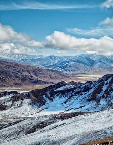 Panoramic view of mountainous terrain with snow and clouds.