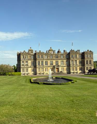 Large historic manor house surrounded by well-maintained gardens.