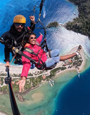 Two people paragliding over a coastal area with clear blue water.