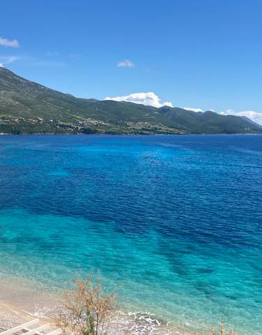 Coastal view with clear blue water and green hills.