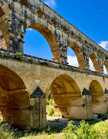 An ancient Roman aqueduct with multiple arches under a bright blue sky.
